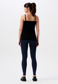 Svart tajt linne med tunna axelband, parat med navy leggings och svarta platåskor. Modellen vänder sig bort från kameran.