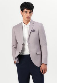 Helles graues Blazer im Slim-Fit, mit einem einreihigen Design, Reverskragen und einem Einstecktuch. Kombiniert mit einem weißen Hemd und dunklen Hosen.