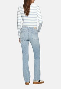 Hellblaue gerade geschnittene Jeans mit mittlerer Leibhöhe, ausgestattet mit Gesäßtaschen und einem Lederlabel am Bund. Das Model trägt ein gestreiftes Oberteil.