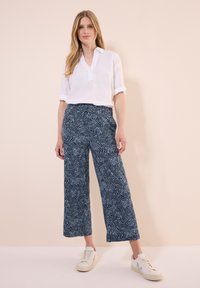 Vit linneskjorta med uppvikta ärmar, tillsammans med marinblå vida byxor med vågmönster. Vita sneakers fulländar outfiten.