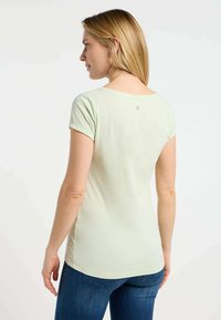 T-shirt di cotone verde chiaro con maniche corte, scollo rotondo e particolare discreto sul retro, abbinato a jeans di denim blu.