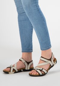 Beige strappy sandals with brown accents; adjustable straps and cushioned footbed; rubber sole for grip; open-toe design.