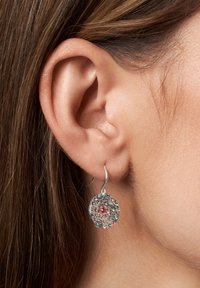 Pendientes circulares de plata con una superficie texturizada, que presentan piedras preciosas de colores en tonos de azul y rosa, colgando de un gancho.