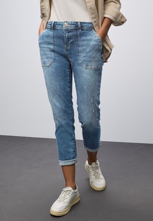 Hellblaue Denim-Cropped-Hosen mit einer ausgewaschenen Optik, umgeschlagenen Säumen und zwei Vordertaschen in geradem Schnitt, ergänzt durch weiße Sneakers.