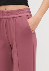 Roze, loszittende broek met een elastische tailleband en zijzakken, gemaakt van zacht, soepel materiaal.