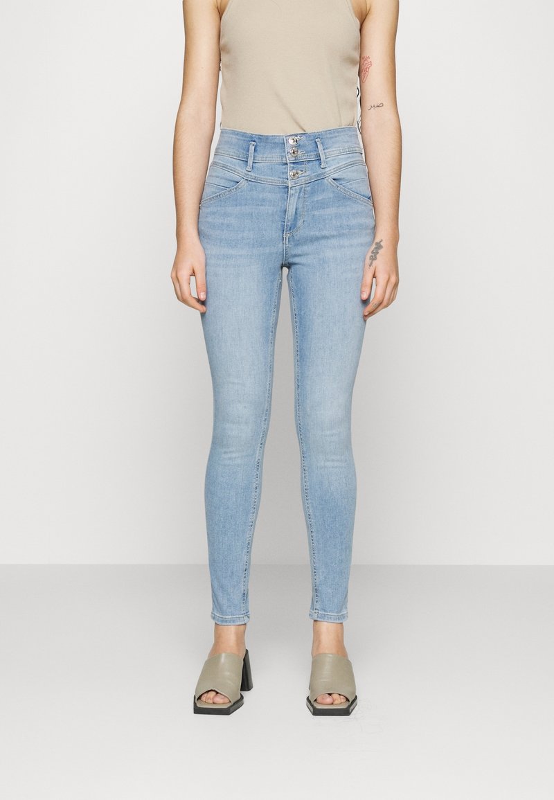 Ljusblå högmidjade skinny jeans i denim. Har framfickor och en flerknäppt stängning. Matchas med beige blockklackar.