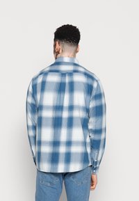 Chemise à carreaux bleue en coton, dotée d'un col boutonné et de manches longues. Remarquable pour son motif à carreaux blanc et bleu clair.