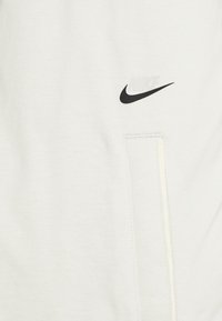 Light gray sweatshirt featuring a visible black Nike logo, a front pocket with a zipper, and soft cotton texture.