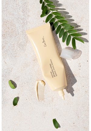 Un tube beige clair avec un embout pointu et un couvercle texturé, étiqueté "Crème Beauté Moringa", placé sur un fond neutre avec des feuilles vertes.