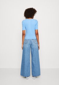 Světle modrý přiléhavý top s krátkým rukávem, spárovaný s volnými světle modrými džíny. Neformální design, měkká textura a minimalistické detaily.