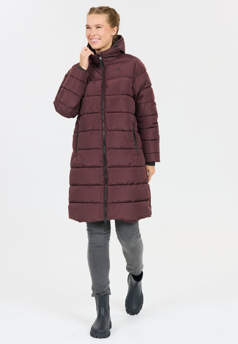Burgundy pufferjacka med hög krage, dragkedja fram och sidofickor, kombinerad med grå byxor och svarta vattentäta stövlar. Slät textur.
