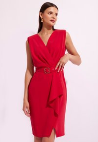 Czerwona sukienka z głębokim dekoltem w kształcie V, bez rękawów, z wcięciem w talii ozdobionym złotą klamrą oraz z plisowanym przodem. Gładka tekstura materiału.