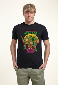 T-shirt in cotone nero con personaggi cartoon colorati delle Tartarughe Ninja, dotata di una stampa grafica vivace e un taglio morbido.