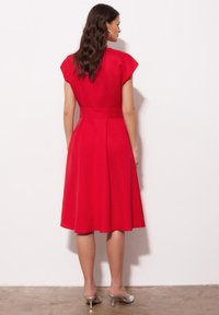 Czerwona sukienka do kolan z krótkimi rękawami, dopasowanym gorsetem, rozkloszowaną spódnicą i podkreśloną talią. Gładki materiał i minimalistyczny design.