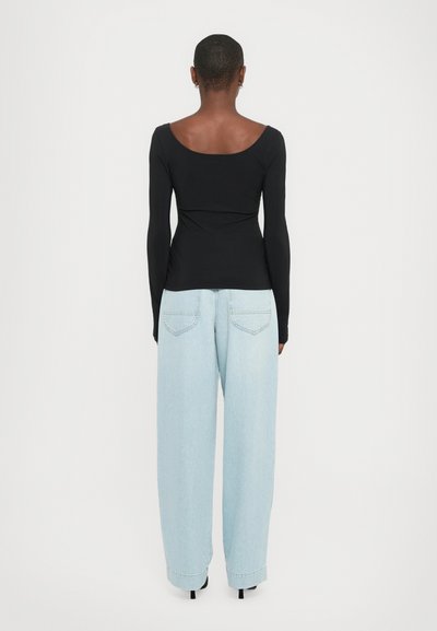 Top nero a maniche lunghe con scollo rotondo, abbinato a jeans a gamba larga di colore blu chiaro, dotati di tasche posteriori e vestibilità comoda.