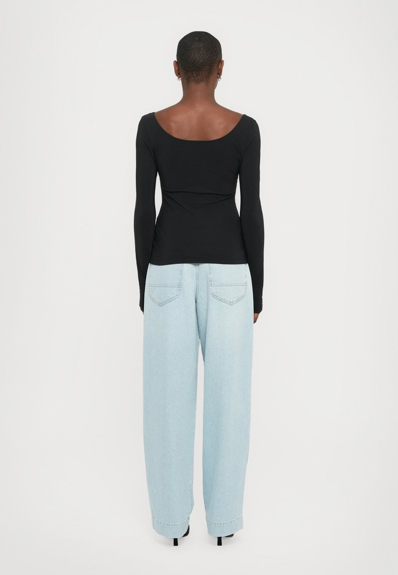 Haut noir à manches longues avec un décolleté en scoop, associé à un jean large bleu clair avec poches arrière et une coupe décontractée.