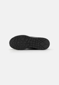 Sorte sneaker såle med en strukturert gummioverflate som har et geometrisk mønster for grep og holdbarhet.