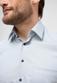 Hellblau karierter Hemd mit strukturiertem Kragen, dunklen Knöpfen und einer Brusttasche, die eine glatte Stoffstruktur betont.