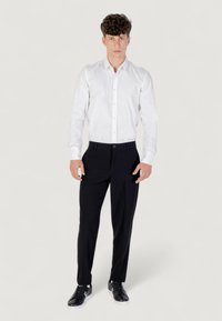 Camicia bianca a bottoni, pantaloni neri, sneakers nere. L'outfit presenta un design classico con una superficie liscia e una vestibilità su misura.