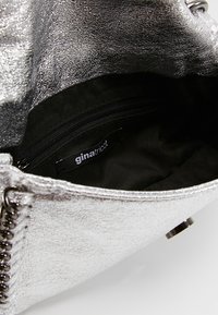 Srebrna metaliczna torebka o fakturowanej powierzchni, zapinana na zamek wewnątrz, z czarną podszewką. Wewnątrz widoczna metka marki.