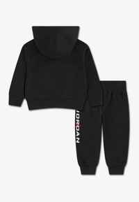 Must kapuutsiga pusa koos sobivate pükstega, millel on soonilised mansetid ja vöökoht. Vasakul püksisäärel on valge ja punase tekstiga "JORDAN".