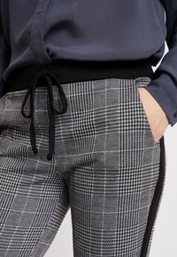 Svart- och vitrutiga byxor med elastisk midja och dragsnöre. Har sidofickor och en kontrasterande svart sidremsa.