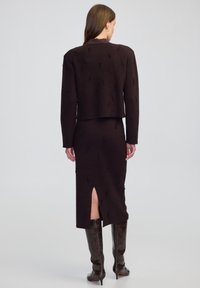 Bruin gebreid tweedelig outfit met een cropped top met textuur en een lange rok met een split aan de achterkant, aangevuld met glanzende laarzen tot de knie.