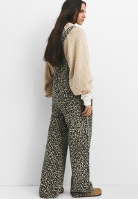 Leopardprint salopettes van een gestructureerde stof met wijde benen, gecombineerd met een crèmekleurige trui met pofmouwen; zijaanzicht.
