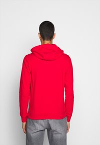 Czerwona bluza z kapturem z przednią kieszenią typu kangurka, długimi rękawami i regulowanym kapturem. Wykonana z miękkiej, elastycznej tkaniny.