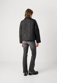 Casaco preto acolchoado com padrão de diamante, gola e mangaslongas, combinado com jeans cinzentos de boca de sino e sapatos pretos robustos.