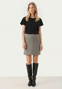 Sort kortærmet t-shirt parret med en ternet nederdel i neutrale toner. Modellen har knæhøje sorte støvler på. Enkel, tætsiddende silhuet.