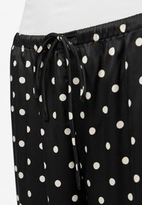 Melni auduma bikses ar lieliem baltiem punktiem. Jostasvieta ir elastīga ar auklu. Gluda tekstūra ar brīvu piegriezumu.