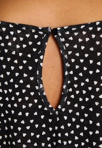 Czarna tkanina w małe białe wzory w serca z łezkowatym wycięciem w kształcie klucza zapinanym na mały czarny guzik.