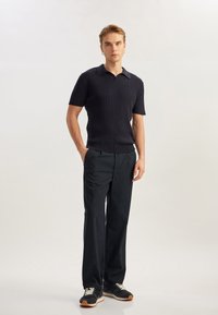 Mörk randig stickad polo med korta ärmar, i kombination med skräddarsydda svarta byxor och mörka sneakers med ljusa snören och gummisulor.