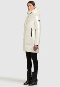 White puffer jacket with a glossy finish, hood, and black zippers. Features a quilted design and side pockets, paired with black leggings and boots.