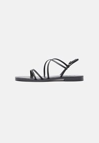 Sandali neri piatti con molteplici cinturini sottili, design elegante, punta aperta e fibbia alla caviglia regolabile. Texture liscia e stile minimalista.