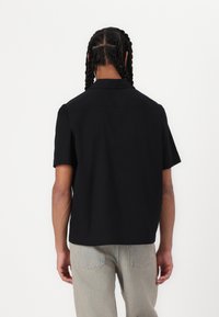 Zwarte t-shirt met korte mouwen en een kraag, met een effen ontwerp, gemaakt van een zacht materiaal. De achterkant toont een rechte snit zonder patronen.