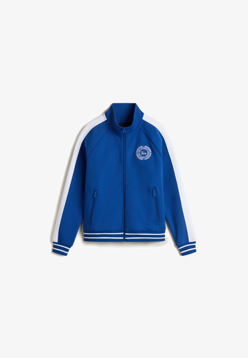 Chaqueta deportiva azul con rayas blancas, cierre de cremallera, dos bolsillos con cremallera y un detalle de logo redondo en el pecho. Textura de tela suave.