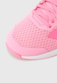 Rosa treningssko med nettoppbygg, glatte tekstilaksenter, flate lisser og hvit mellomsåle; har et sekskantmønster på tåboksen.