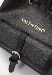 Černá texturovaná kabelka s zlatým logem "VALENTINO", s koženým popruhem a přezkou, což vytváří sofistikovaný vzhled.