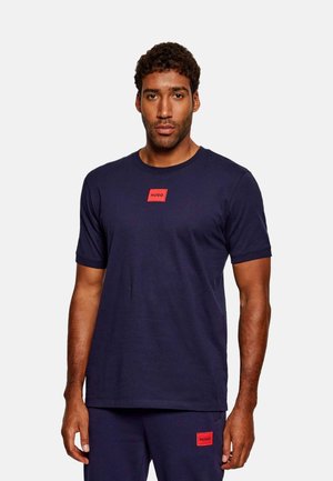 Camiseta de algodón de color azul marino con cuello redondo y mangas cortas. Presenta una pequeña etiqueta rectangular roja con el logotipo "HUGO" en el pecho.