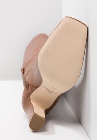 Brązowy skórzany botek na wysokim obcasie o gładkiej fakturze, ze spiczastym noskiem i niskim, szerokim obcasem. Posiada zamek błyskawiczny po boku. Podeszwa jest beżowa.