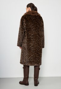 Cappotto di pelliccia con stampa leopardata, caratterizzato da un motivo marrone e nero, una grande collana e una vestibilità comoda. Completato da stivali marroni al ginocchio.