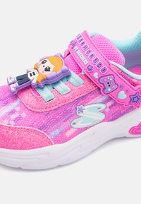 Zapatilla deportiva de color rosa brillante con upper de tela brillante, acentos turquesa, un charm de personaje y una correa de Velcro con adornos de logo.