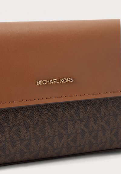 Близък план на кафява чанта Michael Kors с гладък кожен капак, златисто лого и тяло от тъмна шарена материя.