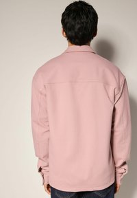 Lyserød sweatshirt med afslappet pasform, lange ærmer, knappede manchetter og en glat tekstur. Bagsiden har en skuldresøm detalje.