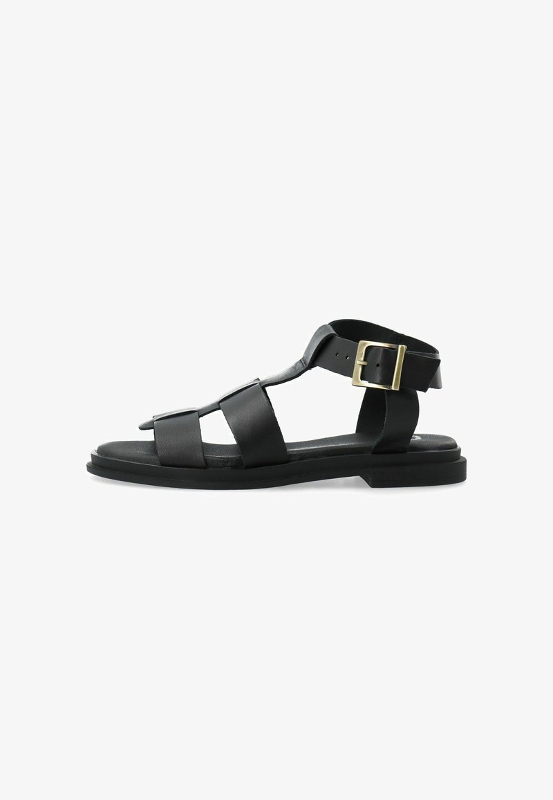 Sandale plate en cuir noir avec trois brides à l'avant, une bride à la cheville et une boucle dorée sur fond blanc.
