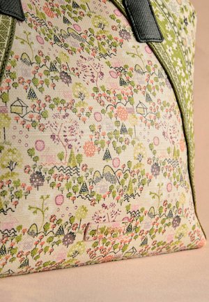 Canvas bag featuring a multicolored floral and geometric print in pink, green, and black, with black leather handles and a textured surface.