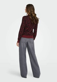 Pull en laine avec motif léopard bordeaux, à manches longues et ourlet côtelé, associé à un pantalon gris à jambes larges. La texture du pull est tricotée.