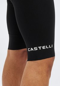 Κοντινό πλάνο του μηρού ενός ατόμου που φοράει μαύρο ποδηλατικό σορτς με το λευκό λογότυπο "CASTELLI" τυπωμένο κοντά στο τελείωμα.